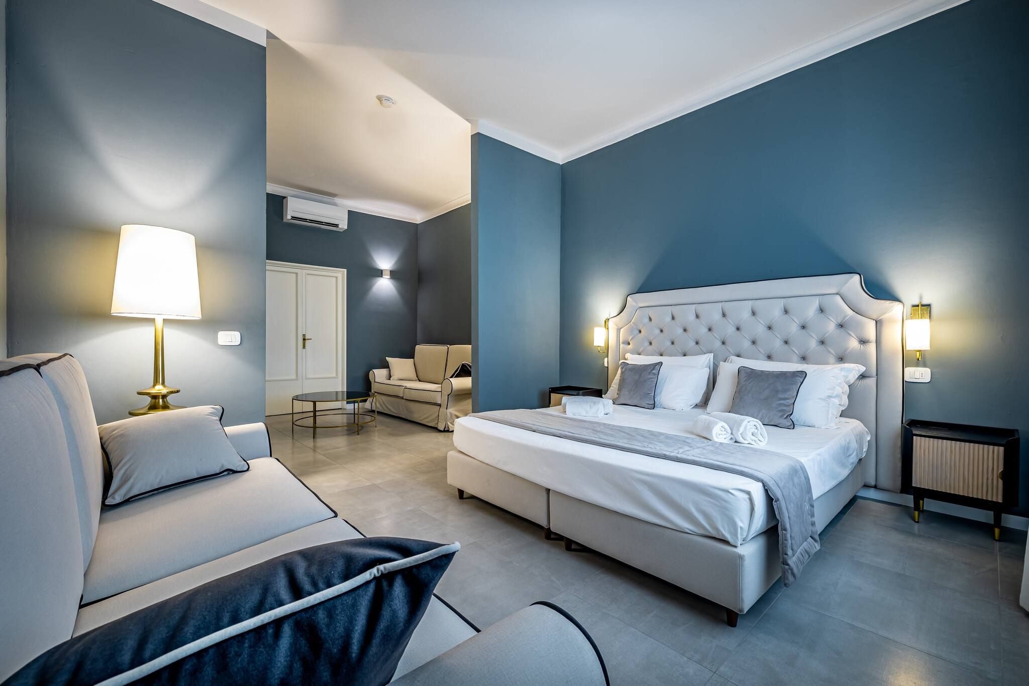A modern bedroom with a large bed, a sofa, a chair, and a bedside table.