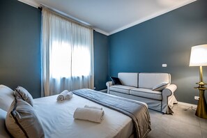 Ein Hotelzimmer mit Bett, Sofa, Lampe und einem Fenster mit Vorhängen.