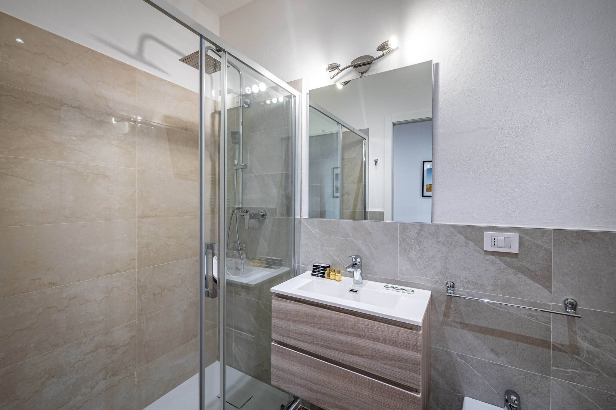 Un baño moderno con cabina de ducha de vidrio, tocador con espejo y toallero.