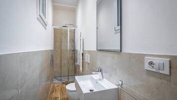 Ein modernes Badezimmer mit einer Duschkabine aus Glas, einem weißen Waschbecken und einer Toilette.