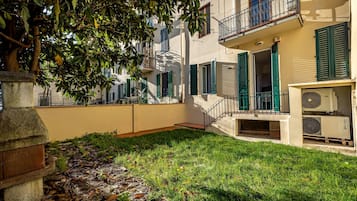 A courtyard with a stone bench, a tree, and a building with green shutters and a balcony.