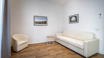 Una sala de estar moderna con un sofá blanco, un sillón blanco y una pequeña mesa redonda. Dos cuadros enmarcados decoran las paredes.