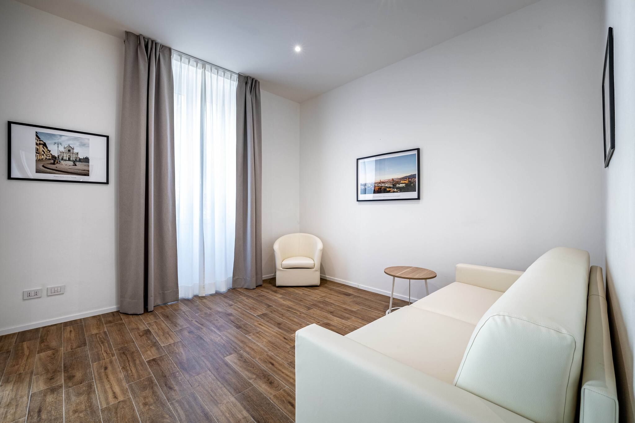 Un salon moderne avec un canapé blanc, une petite table ronde, un fauteuil beige et deux tableaux encadrés accrochés aux murs.
