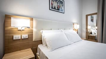 A hotel room with a wooden headboard, a large bed with white linens, bedside lamps, a nightstand, and a framed picture on the wall.