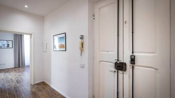 Un pasillo con suelo de madera, paredes blancas y una puerta cerrada con sistema de seguridad.