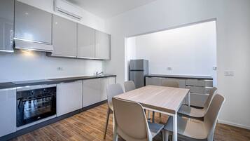 Una cocina moderna con armarios blancos, horno empotrado y comedor con mesa y sillas de madera.