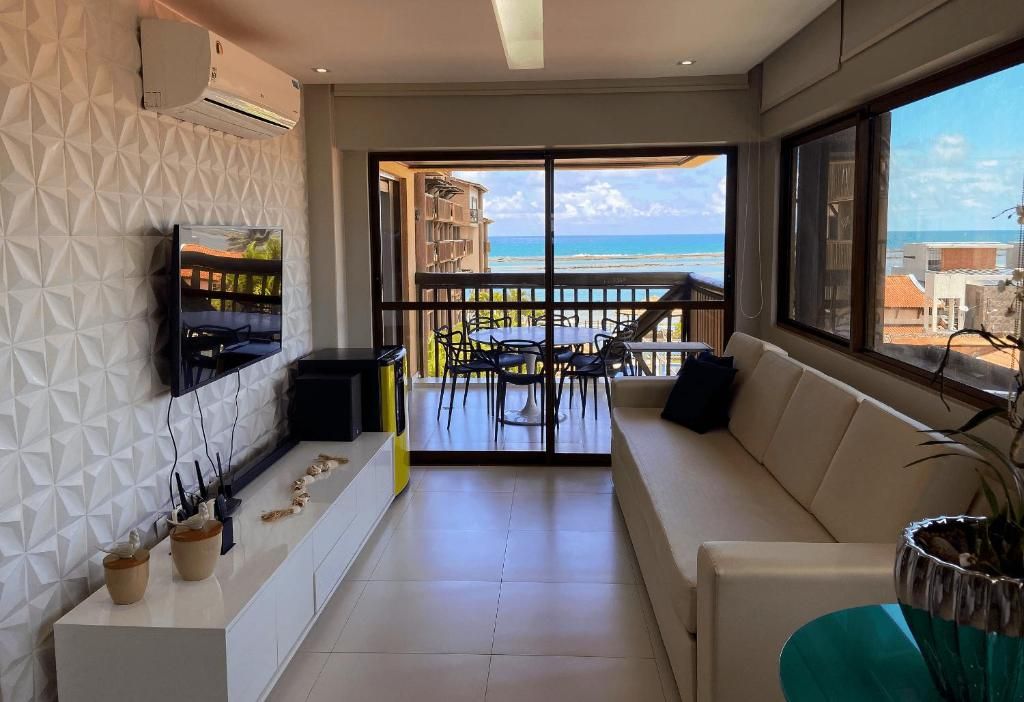 Ein modernes Wohnzimmer mit Balkon und Meerblick, einem Wand-Fernseher und einem Essbereich mit Stühlen und Tisch.