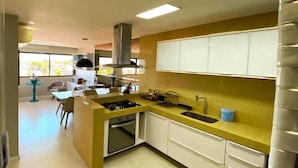 A modern kitchen with a central island, white cabinets, and a yellow countertop. - Cobertura Vista Mar Barra Bali (Barra de São Miguel)