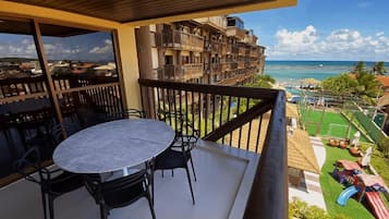 A balcony with a table and chairs, overlooking a beach and a children's play area.