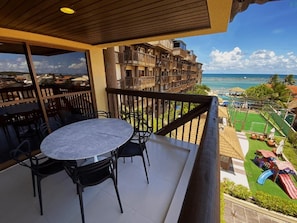 Un balcón con una mesa y sillas, con vista a una playa y una zona de juegos infantiles.