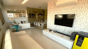 A modern living room with a sofa, a TV, and a yellow appliance. - Cobertura Vista Mar Barra Bali (Barra de São Miguel)