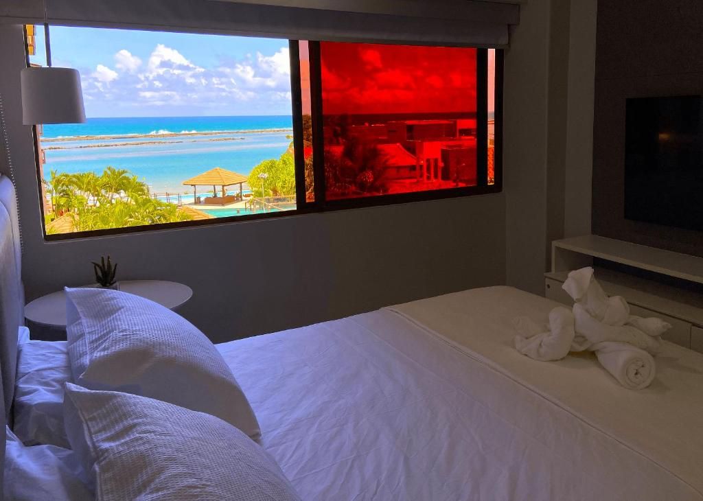Quarto de hotel com cama, televisão, janela com vista para a praia e uma pequena mesa com uma planta.