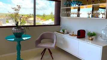 A room with a view of a cityscape through large windows, a teal table with a potted plant, a white cabinet with glassware, and a pink chair.
