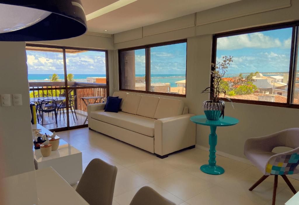 A modern living room with a sofa, a dining table, and chairs. There is a balcony with a view of the ocean.