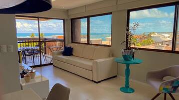 Uma sala de estar moderna com um sofá, uma mesa de jantar e cadeiras. Há uma varanda com vista para o oceano.
