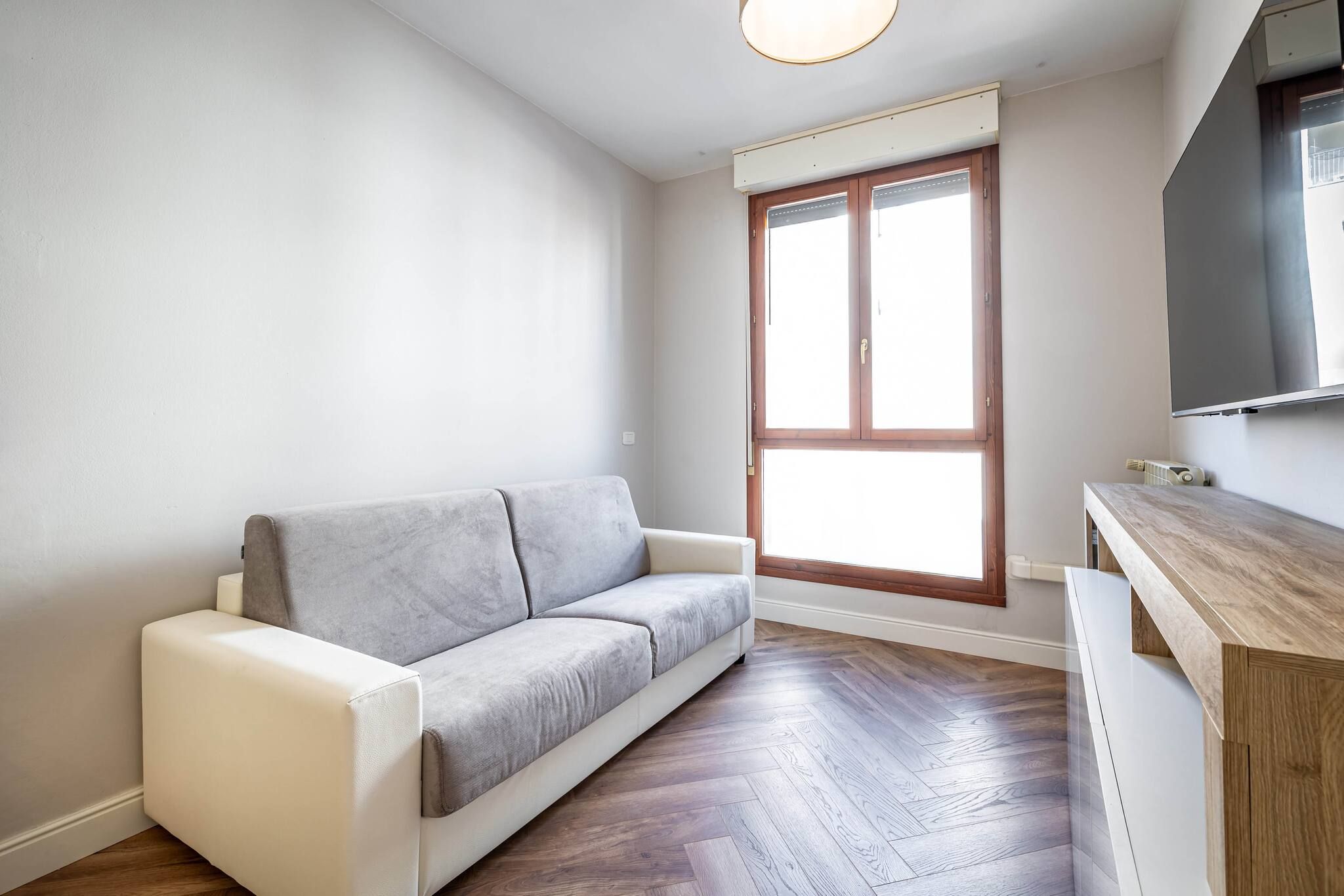A modern living room with a grey sofa, wooden flooring, and a large window.