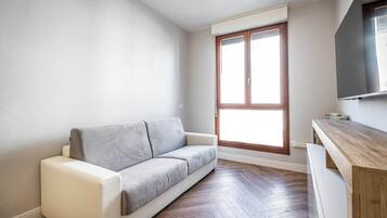 A modern living room with a grey sofa, wooden flooring, and a large window.