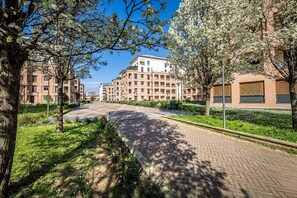 A residential area with multi-story apartment buildings, a paved pathway, and trees with white blossoms. - Castelnuovo Tedesco (Florence)