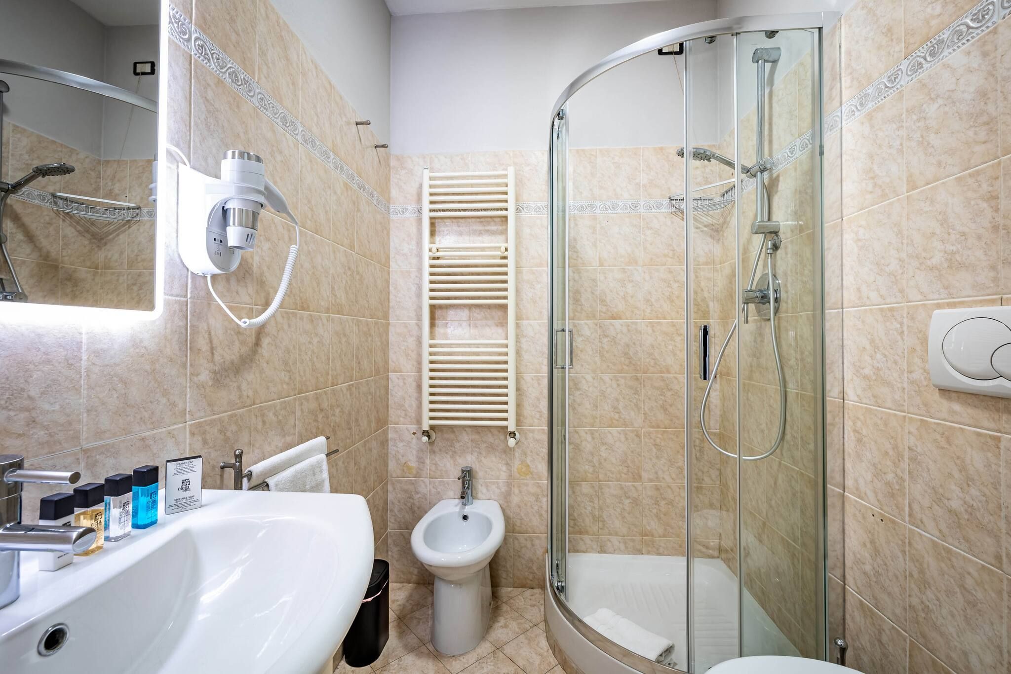 A modern bathroom with a glass-enclosed shower, a pedestal sink, and a bidet.