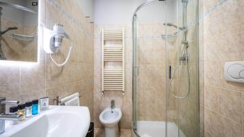 A modern bathroom with a glass-enclosed shower, a pedestal sink, and a bidet.