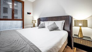 A neatly made bed with a grey blanket, two pillows, and a wooden headboard. There is a bedside table with a lamp and a wall-mounted alarm clock. - Castelnuovo Tedesco (Florence)