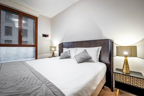A neatly made bed with a grey blanket, two pillows, and a wooden headboard. There is a bedside table with a lamp and a wall-mounted alarm clock. - Castelnuovo Tedesco (Florence)