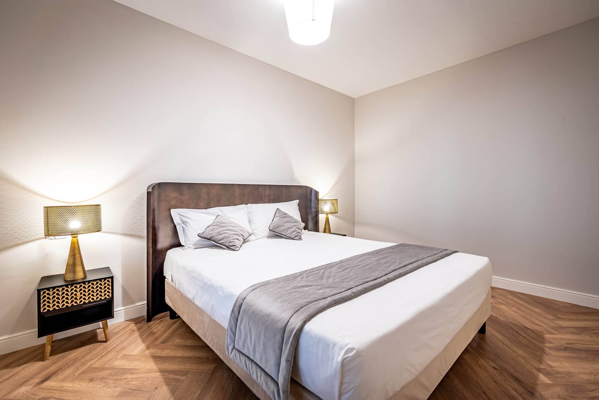 A bedroom with a bed, two bedside tables with lamps, and a wooden floor.