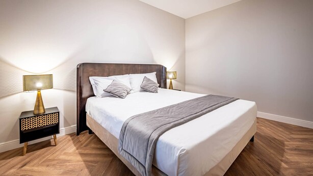 A bedroom with a bed, two bedside tables with lamps, and a wooden floor. - Castelnuovo Tedesco (Florence)