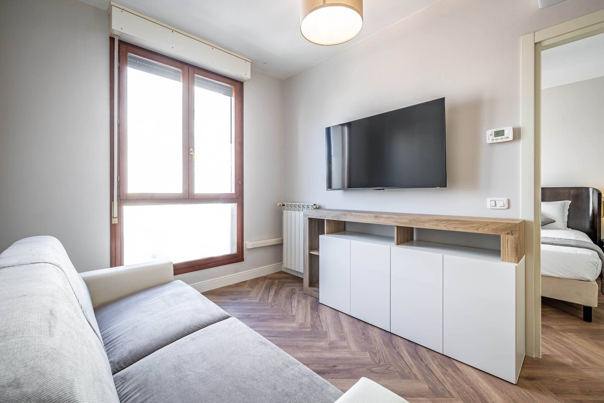 A modern living room with a sofa, a TV mounted on the wall, a wooden console table, and a bed with a headboard.
