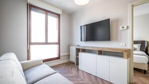 A modern living room with a sofa, a TV mounted on the wall, a wooden console table, and a bed with a headboard. - Castelnuovo Tedesco (Florence)