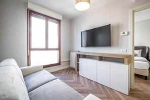 A modern living room with a sofa, a TV mounted on the wall, a wooden console table, and a bed with a headboard. - Castelnuovo Tedesco (Florence)
