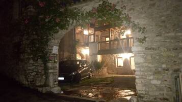 A stone building with a car parked in front, a balcony, and a small garden area.