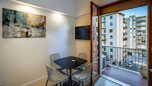 A modern apartment with a balcony, a dining area with a table and chairs, a large abstract painting, and a TV mounted on the wall. - Pasquini (Florence)