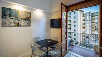 A modern apartment with a balcony, a dining area with a table and chairs, a large abstract painting, and a TV mounted on the wall.