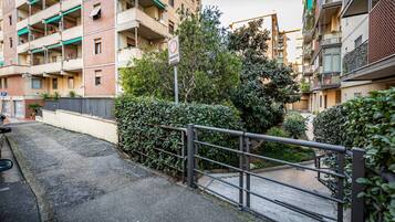 Un edificio residencial con balcones, entrada protegida por un portón y un sendero pavimentado.