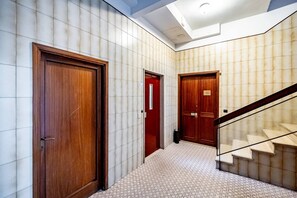 Un couloir aux murs ornés de motifs, doté de portes en bois et d’un escalier avec une rampe en verre.