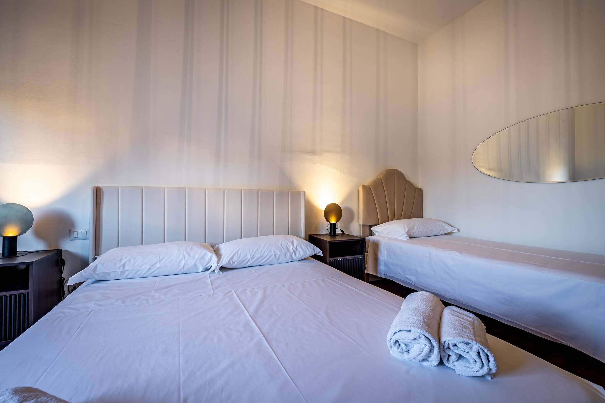 A hotel room with two beds, a nightstand with lamps, and a large mirror on the wall.
