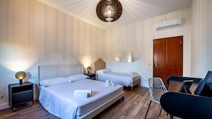 A hotel room with two beds, a wooden door, a wall-mounted air conditioner, a modern pendant light, and a small table with chairs. - Pasquini (Florence)