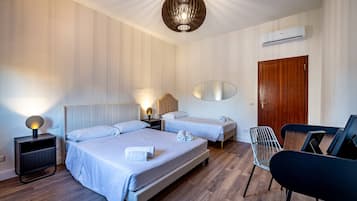 A hotel room with two beds, a wooden door, a wall-mounted air conditioner, a modern pendant light, and a small table with chairs.