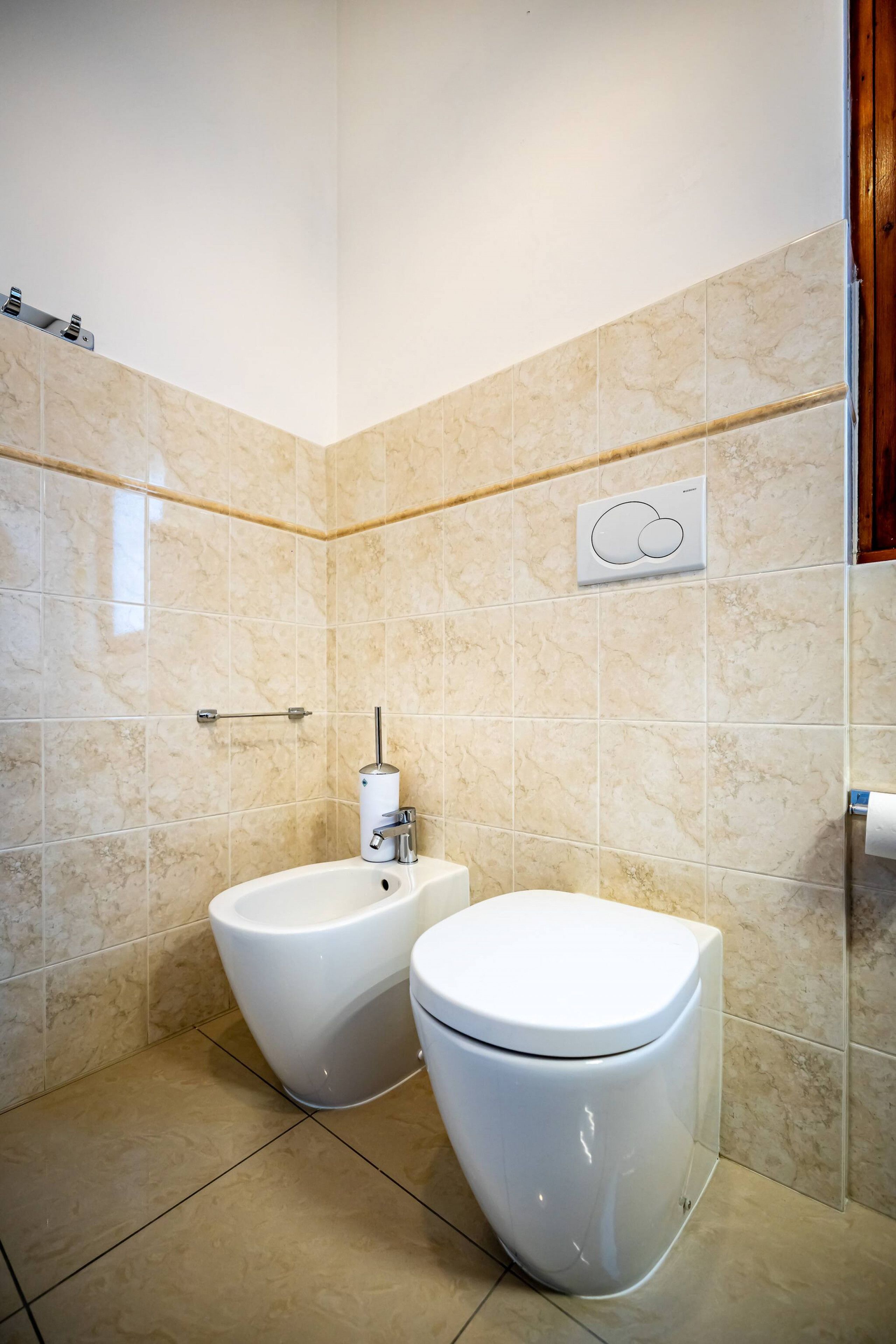 Et moderne badeværelse med to toiletter, en bidet og en håndklædestang.