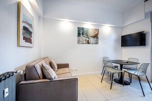En moderne stue med sofa, spisebord med stole, et fladskærms-tv monteret på væggen og billeder på væggene.