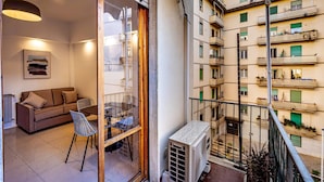 A balcony with a view of a residential building, a table with chairs, and a sofa inside a room. - Pasquini (Florence)