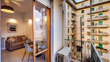 A balcony with a view of a residential building, a table with chairs, and a sofa inside a room.