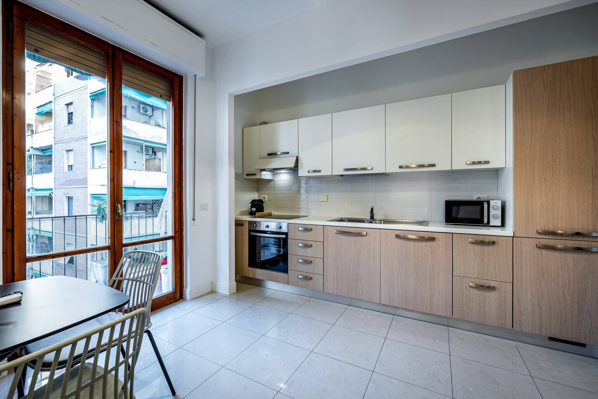 Una cocina moderna con comedor, ventanas amplias y vista a un edificio residencial.