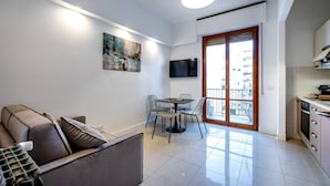 A modern living room with a sofa, dining table, and chairs. There is a TV mounted on the wall and a balcony with a view of the city. - Pasquini (Florence)
