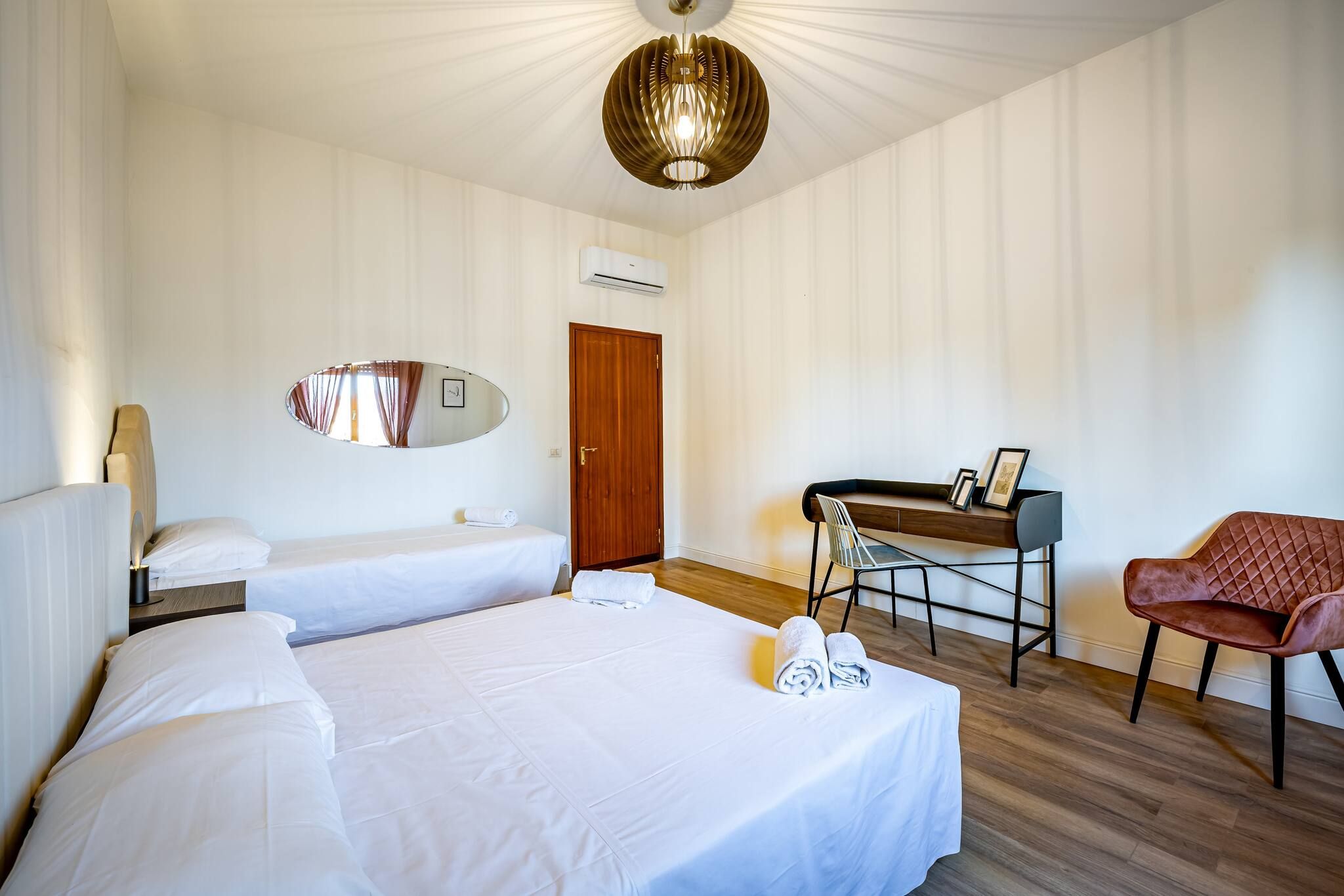 A hotel room with two beds, a desk, a chair, and a mirror.