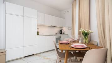 A modern kitchen with white cabinets, a dining table set with pink plates and glasses, and a vase of flowers.