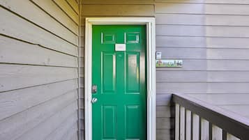 Una puerta verde con cerradura electrónica, un buzón y una barandilla de madera en el porche.