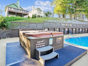Un bain à remous agrémenté d’un panneau d’avertissement, une piscine et une clôture en bois avec des chaises.