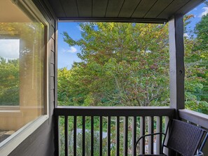A covered porch with a view of trees and a chair. - First Cub 1301 (Gatlinburg)